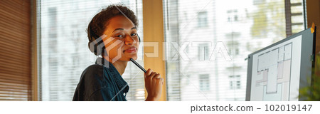 Smiling Afro american woman interior designer in headphones works with documents in home office Smiling Afro american woman interior designer in headphones works with documents in home office 102019147