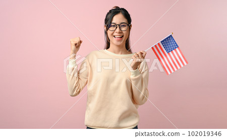 Confident Asian girl showing a USA flag on pink isolated background, education concept. 102019346