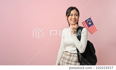 Cheerful young Asian woman showing a Malaysia flag on pink isolated background 102019357
