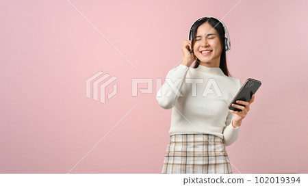 Happy young female listening to music with her headphone, on pink isolated background. 102019394