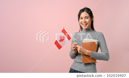 Confident Asian girl showing Canada flag on pink isolated background, education concept 102019407