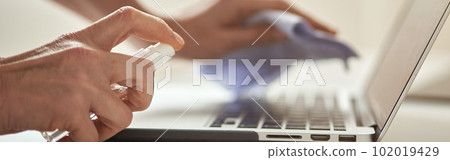 Close up shot of female hands using antibacterial sanitizer spray while disinfecting laptop keyboard 102019429