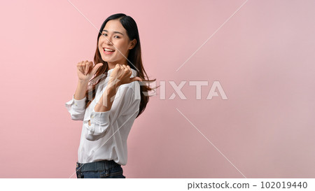 A woman wearing white shirt pointing finger to the side on pink isolated background. 102019440