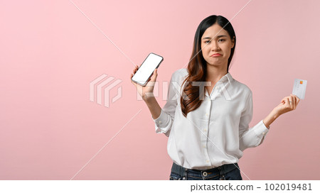 Confident Asian woman holding her smartphone and credit card, isolated on pink background 102019481