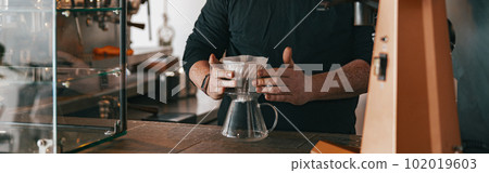 Men barista making a drip filter coffee standing by counter in coffeeshop Men barista making a drip filter coffee standing by counter in coffeeshop 102019603