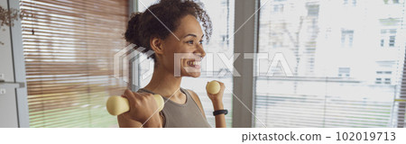 Smiling woman with dumbbells doing exercising at home and working on arms strength Smiling woman with dumbbells doing exercising at home and working on arms strength 102019713