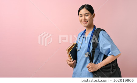 Portrait of young female medical student smiling to the camera while holding textbooks Portrait of young female medical student smiling to the camera while holding textbooks 102019906