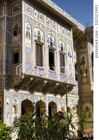 Colourful paintings and wooden windows on the outer wall of Seth Harmukhrai Sanehiram Chokhani Double Haveli, located in Mandawa, Shekhawati, Rajasthan, India 102023481