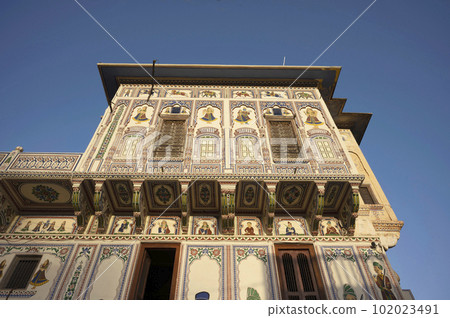 Colourful paintings on the outer wall of an entrance of Seth Harmukhrai Sanehiram Chokhani Double Haveli, located in Mandawa, Shekhawati, Rajasthan, India 102023491