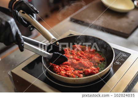 Close up of chef in uniform is cooking dish on frying pan for client order on restaurant kitchen Close up of chef in uniform is cooking dish on frying pan for client order on restaurant kitchen 102024035