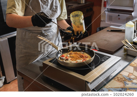 The professional chef in uniform adds spices into pan with dish in restaurant kitchen 102024260