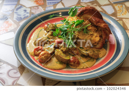 Tasty croissant filled with omelet with fried vegetables and sauce served on plate for breakfast 102024346