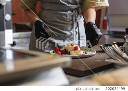 Kitchen worker decorated ready cheesecakes with berries for breakfast in restaurant Kitchen worker decorated ready cheesecakes with berries for breakfast in restaurant 102024499