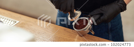 Woman is holding portafilter and coffee tamper 102024773