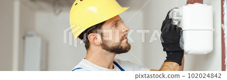 Focused professional heating fitter checking gas consumption at gas pipe and meter counter 102024842
