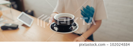 Female barista offering cup of coffee in cafeteria 102024884