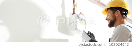 Low angle view of technician, heating fitter in hard hat and protective gloves making notes while checking gas consumption at gas pipe and meter counter 102024942