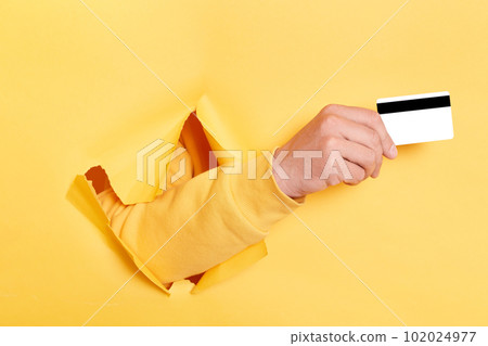 Image of person hand breaking through yellow paper and holding credit card, recommend bank or shopping discounts, earning money, banking. 102024977