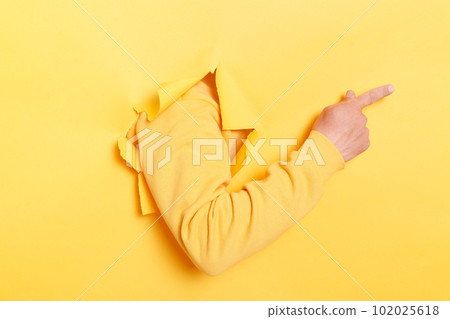Faceless human breaks arm through paper yellow wall indicates on right at blank space, gives advice to buy subscription, suggests to click on link, showing direction. Place for your advertisement Faceless human breaks arm through paper yellow wall indicates on right at blank space, gives advice to buy subscription, suggests to click on link, showing direction. Place for your advertisement 102025618