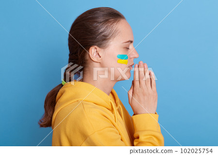 Side view portrait of depressed sad upset dark haired woman, praying for Ukrainians, stop war between Russia and Ukraine. Stay with Ukraine. Glory to Ukraine. Side view portrait of depressed sad upset dark haired woman, praying for Ukrainians, stop war between Russia and Ukraine. Stay with Ukraine. Glory to Ukraine. 102025754