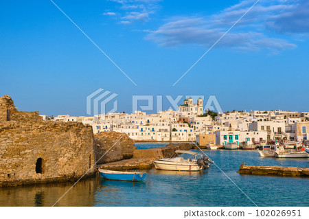 Greek whitewashed houses, old castle and church by harbour waterfront on sunny day, Naoussa, Paros island, Greece 102026951