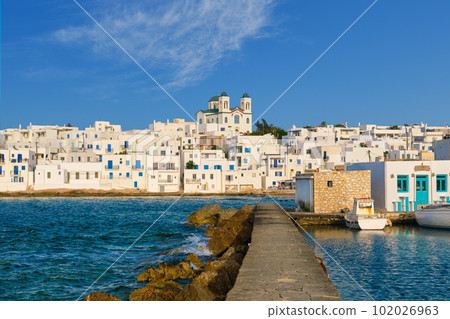 Greek whitewashed houses and church by harbour watersfront on sunny day, Naoussa, Paros island, Greece 102026963