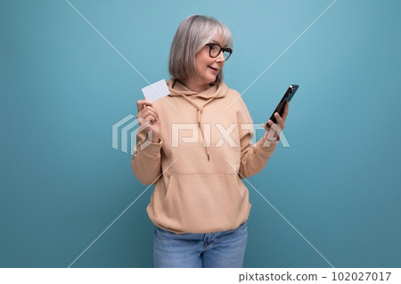 60s granny woman with gray hair who masters cashless payments by credit card on a studio background 102027017