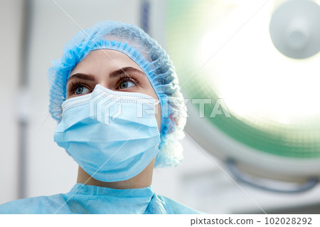 Close-up image of young woman, doctor, surgeon in protective medical mask, uniform leading surgery in medical clinic, hospital in surgery room Close-up image of young woman, doctor, surgeon in protective medical mask, uniform leading surgery in medical clinic, hospital in surgery room 102028292