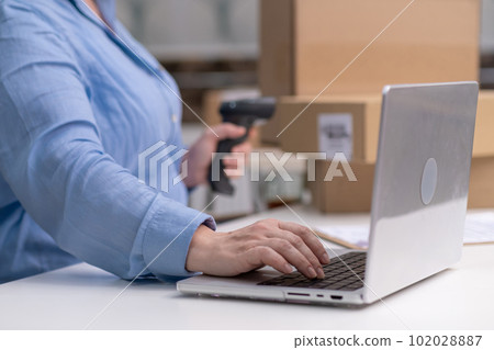woman hands checking online orders on laptop managing receipts and invoices for online shop. using barcode scanner for packages boxes 102028887