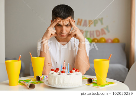 Horizontal shot of sad pensive man alone preparing birthday party, thinking about guests. keeping hands on temples, sitting at the table with upset facial expression. Horizontal shot of sad pensive man alone preparing birthday party, thinking about guests. keeping hands on temples, sitting at the table with upset facial expression. 102030289