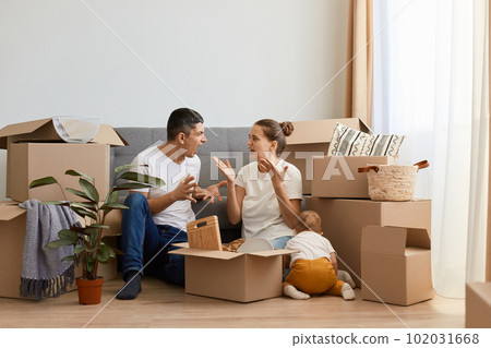 Indoor shot of sad aggressive couple having argument while moving to a new house, sitting on floor near sofa and screaming, quarelling during relocation in a new apartment. Indoor shot of sad aggressive couple having argument while moving to a new house, sitting on floor near sofa and screaming, quarelling during relocation in a new apartment. 102031668
