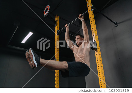 Muscular athlete doing abs exercise on horizontal bar 102031819