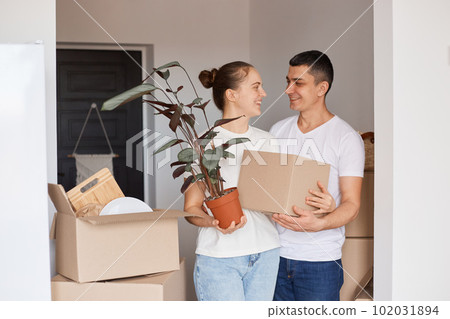 Portrait of happy family standing with boxes and plant in flower pot, looking at each other with gentle and love, being glad to buy a new house, relocating, property, real estate. Portrait of happy family standing with boxes and plant in flower pot, looking at each other with gentle and love, being glad to buy a new house, relocating, property, real estate. 102031894