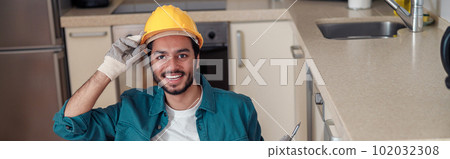 Smiling professional worker in uniform is assembling furniture on kitchen. Repair concept Smiling professional worker in uniform is assembling furniture on kitchen. Repair concept 102032308