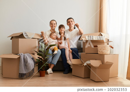 Indoor shot of happy positive family sitting on sofa with children surrounded with carton boxes, father showing to camera keys of their new apartment. Indoor shot of happy positive family sitting on sofa with children surrounded with carton boxes, father showing to camera keys of their new apartment. 102032353