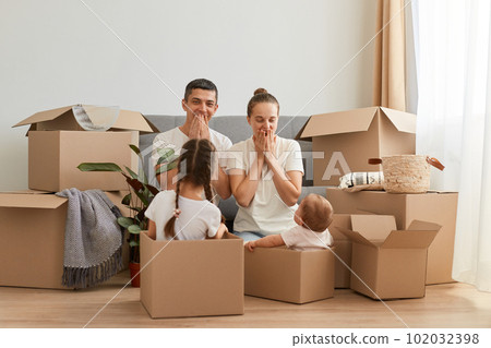 Portrait of happy excited family, woman and man with their children sitting on floor with excited surprised facial expression, kids in cardboard boxes, relocating in a new house. Portrait of happy excited family, woman and man with their children sitting on floor with excited surprised facial expression, kids in cardboard boxes, relocating in a new house. 102032398