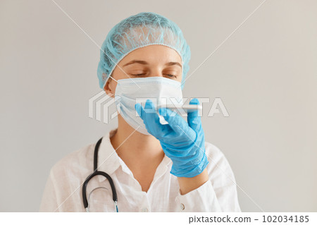 Indoor shot of Caucasian female doctor or nurse wearing medical uniform, posing with stethoscope, holding mobile phone in hands, recording voice message. 102034185