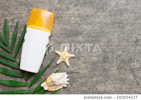 Sunscreen spray bottle. Bottle with sun protection cream and sea shells with tropical green leaf on color background, top view 102034227