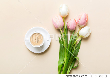 Spring background with flowers, a cup of coffee and a bouquet of pink and white tulips on colored table background with place for text. Copy space top view 102034331