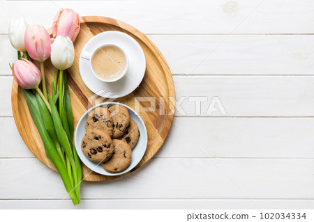 Cup of coffee mug with coffee, cookies and tulips on a colored background. Greeting spring card top view Cup of coffee mug with coffee, cookies and tulips on a colored background. Greeting spring card top view 102034334