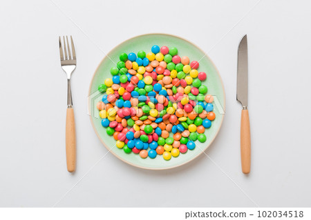 cutlery on table and sweet plate of candy. Health and obesity concept, top view on colored background 102034518