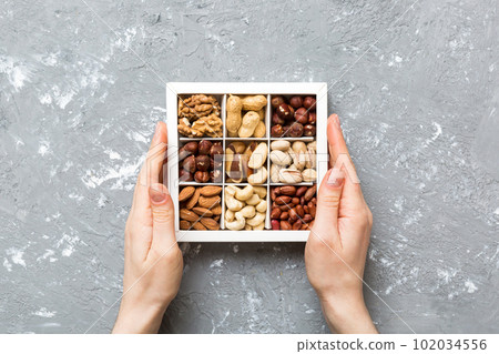 Young woman holding box with different nuts, closeup. Close up, copy space, top view, flat lay. Walnut, pistachios, almonds, hazelnuts and cashews Young woman holding box with different nuts, closeup. Close up, copy space, top view, flat lay. Walnut, pistachios, almonds, hazelnuts and cashews 102034556