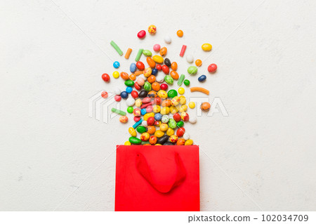 shopping paper gift bag in corner full of assorted traditional candies falling out on colored background with copy space. Happy Holidays sale concept shopping paper gift bag in corner full of assorted traditional candies falling out on colored background with copy space. Happy Holidays sale concept 102034709