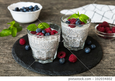 Healthy breakfast or morning with chia seeds vanilla pudding raspberry and blueberry berries on table background, vegetarian food, diet and health concept. Chia pudding with raspberry and blueberry 102034802