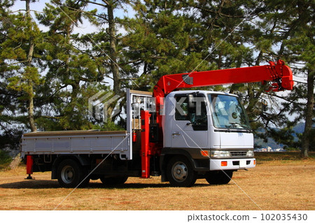 A truck with a simple crane parked in a pine forest A truck with a simple crane parked in a pine forest 102035430