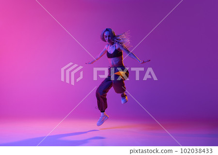 One dancer, woman wearing casual clothes jumping up in motion over gradient purple neon background. Improvisation One dancer, woman wearing casual clothes jumping up in motion over gradient purple neon background. Improvisation 102038433