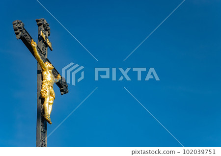 A iron cross with the crucified Jesus Christ on a background of blue sky A iron cross with the crucified Jesus Christ on a background of blue sky 102039751
