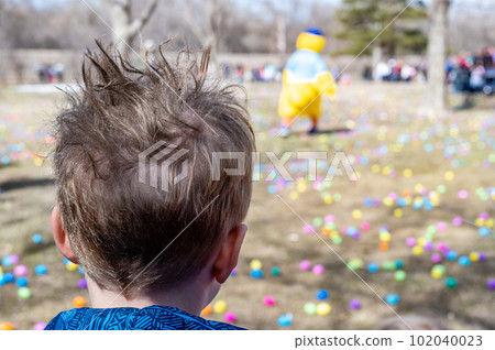 Selective focus on a single child looking out over a field of plastic Easter eggs at a public hunting event. 102040023