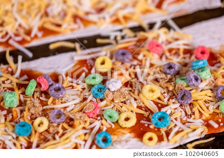 Pizza made by a child with cereal, cheese, and sauce. 102040605