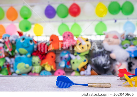 selective focus on darts sitting on a ledge with a wall of balloon targets and prizes that a player can win at a fair. selective focus on darts sitting on a ledge with a wall of balloon targets and prizes that a player can win at a fair. 102040666